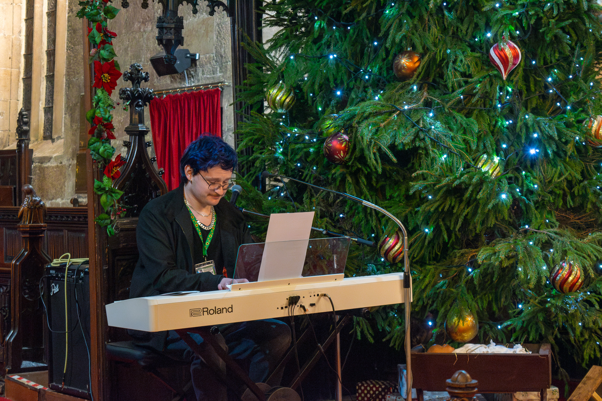 A young man from one of the schools is joyfully playing the piano next to a beautifully decorated Christmas tree