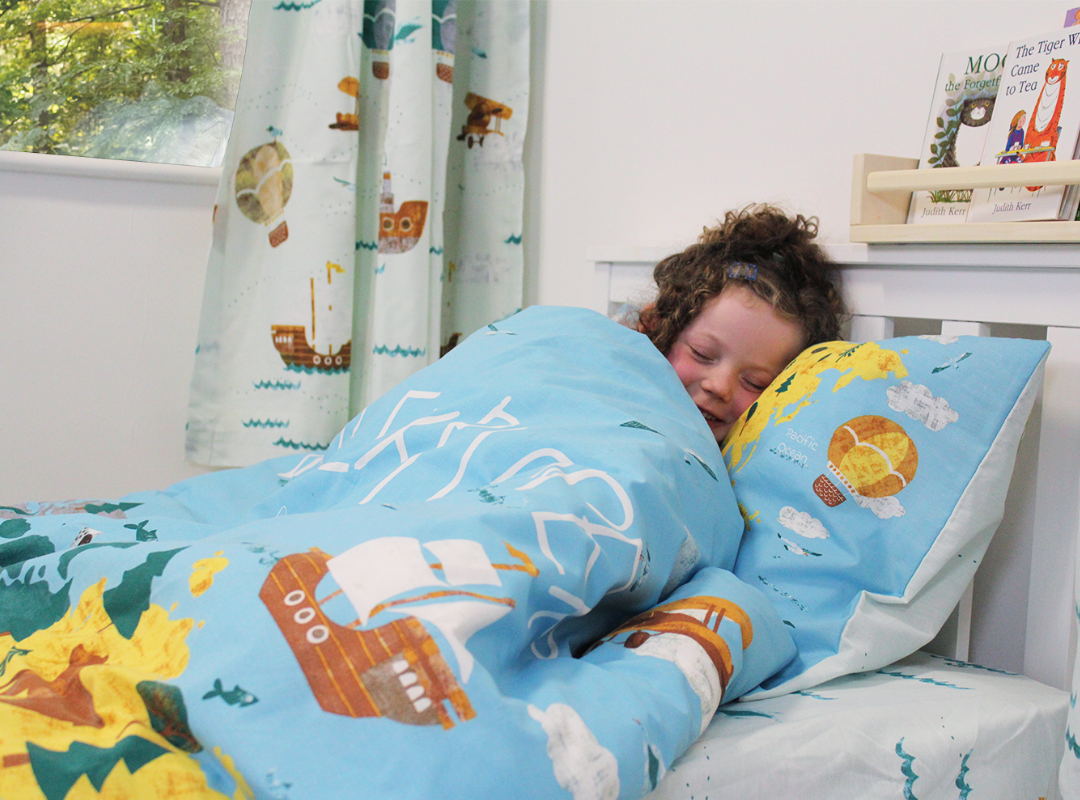 Young girl sleeping in a bed with travel themed bedding and curtains. 