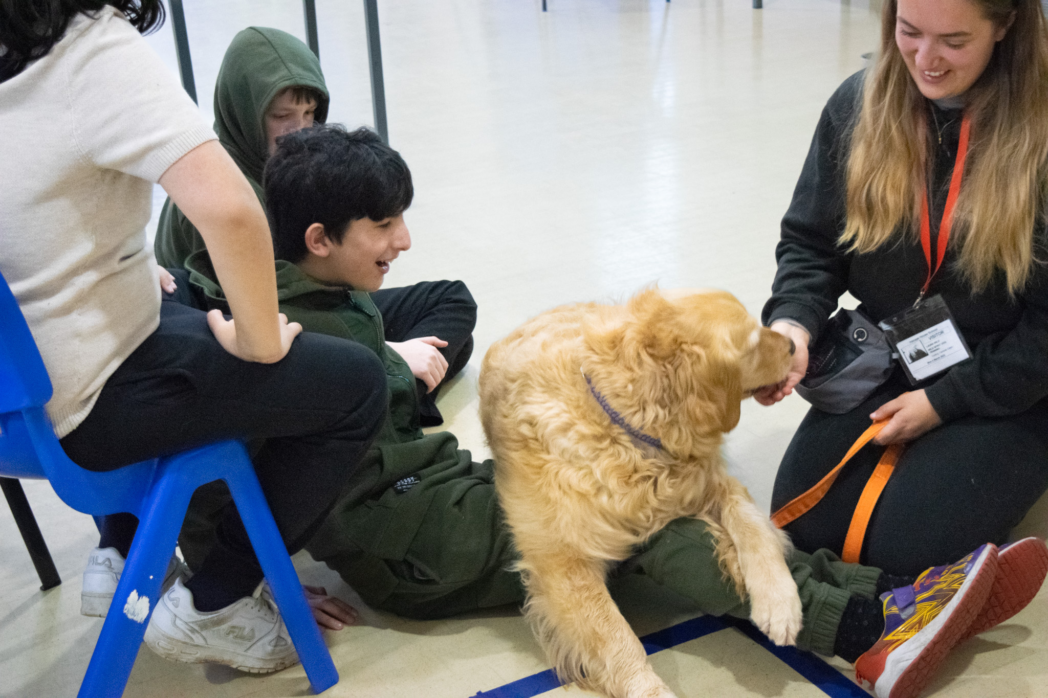 A boy is laughing as the golden retriever lies on top of his legs whilst sat on the floor.
