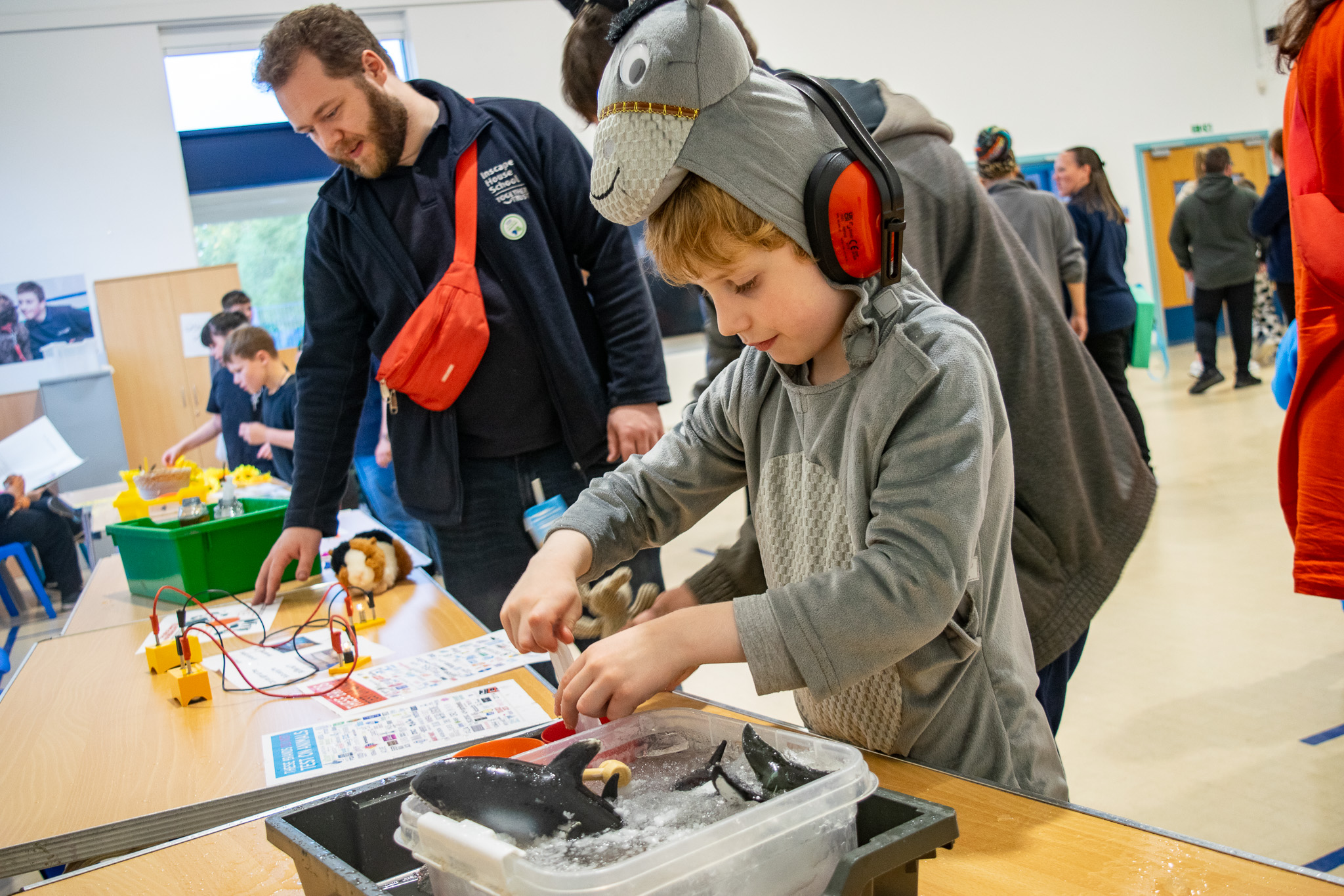 a boy wearing a donkey onesie playing in a tub where a few toy orcas are stuck in ice 