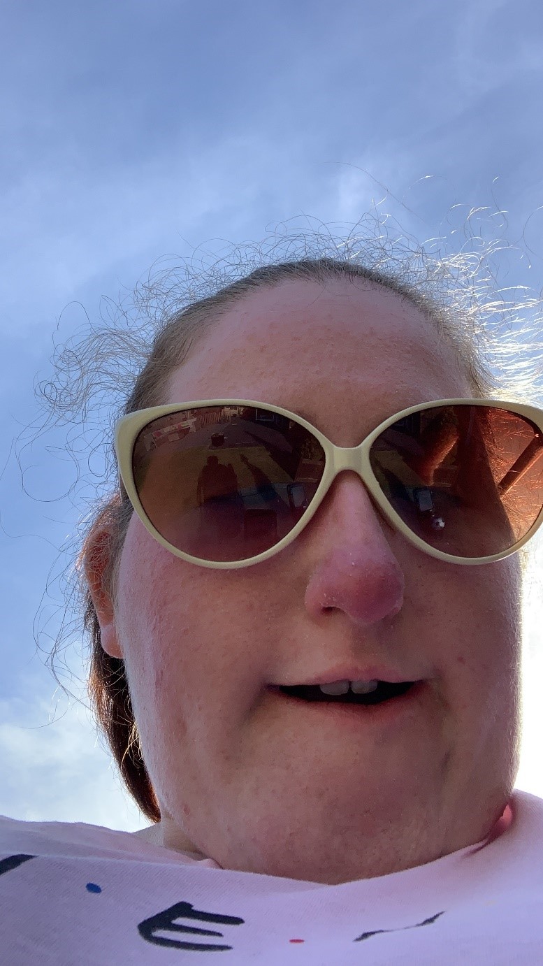 A selfie of Greer wearing sunglasses with a blue sky behind her