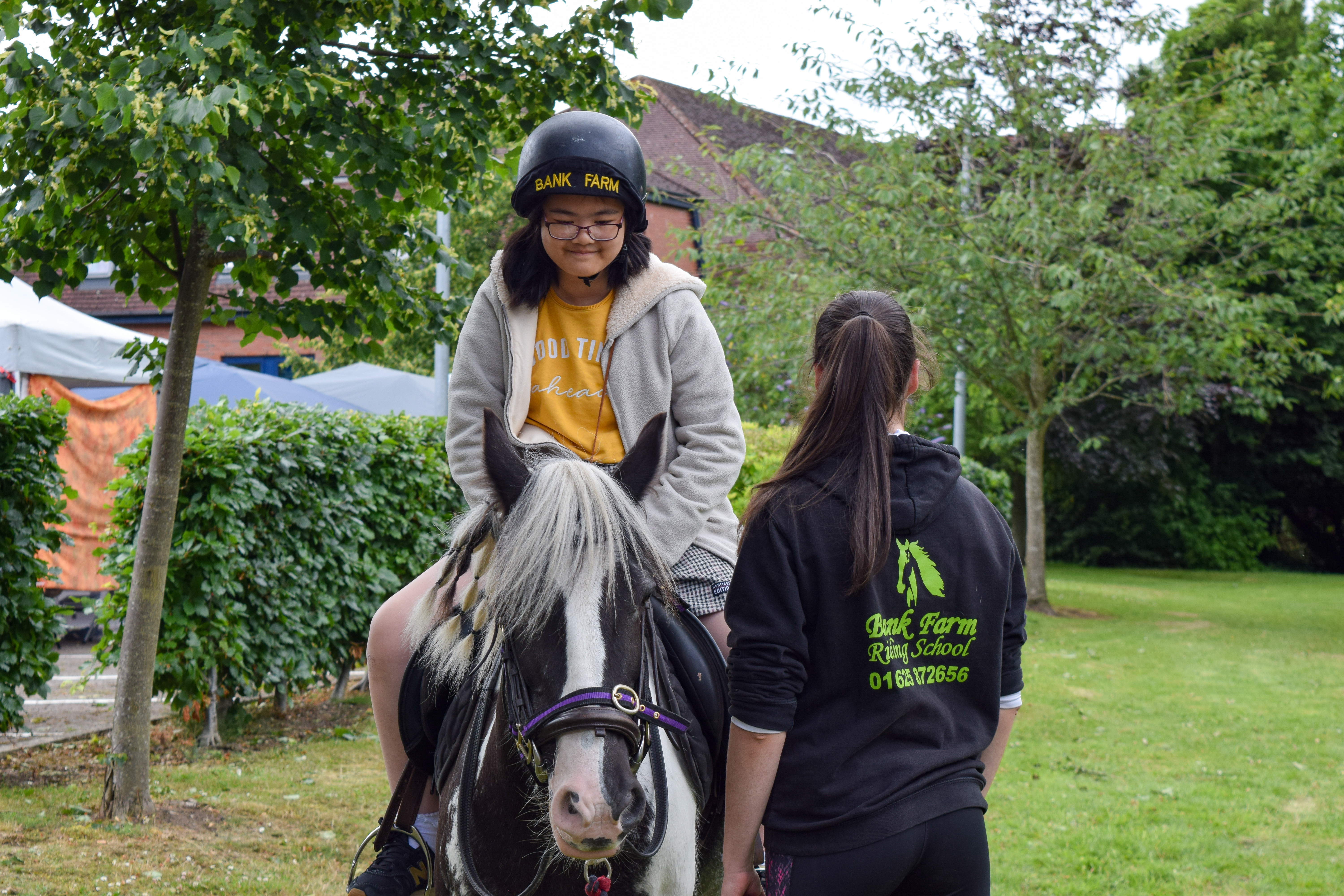 A small girl wearing a helmet and riding a pony with an animal assistant next to her.