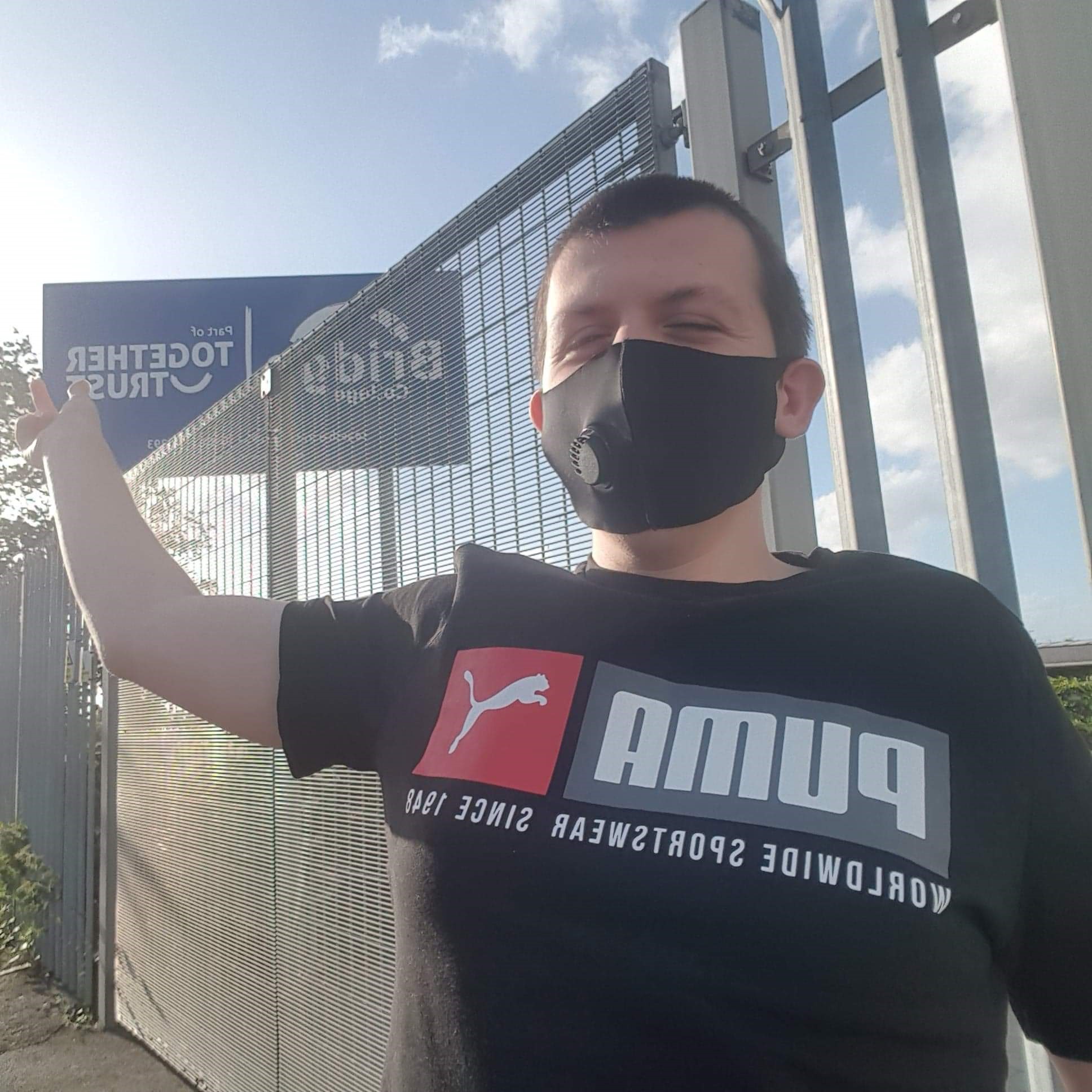 A photo of Liam outside Bridge College pointing at the sign. He is wearing a face mask.