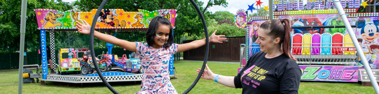 young girl posing on an aerial hoop next to an instructor smiling at her
