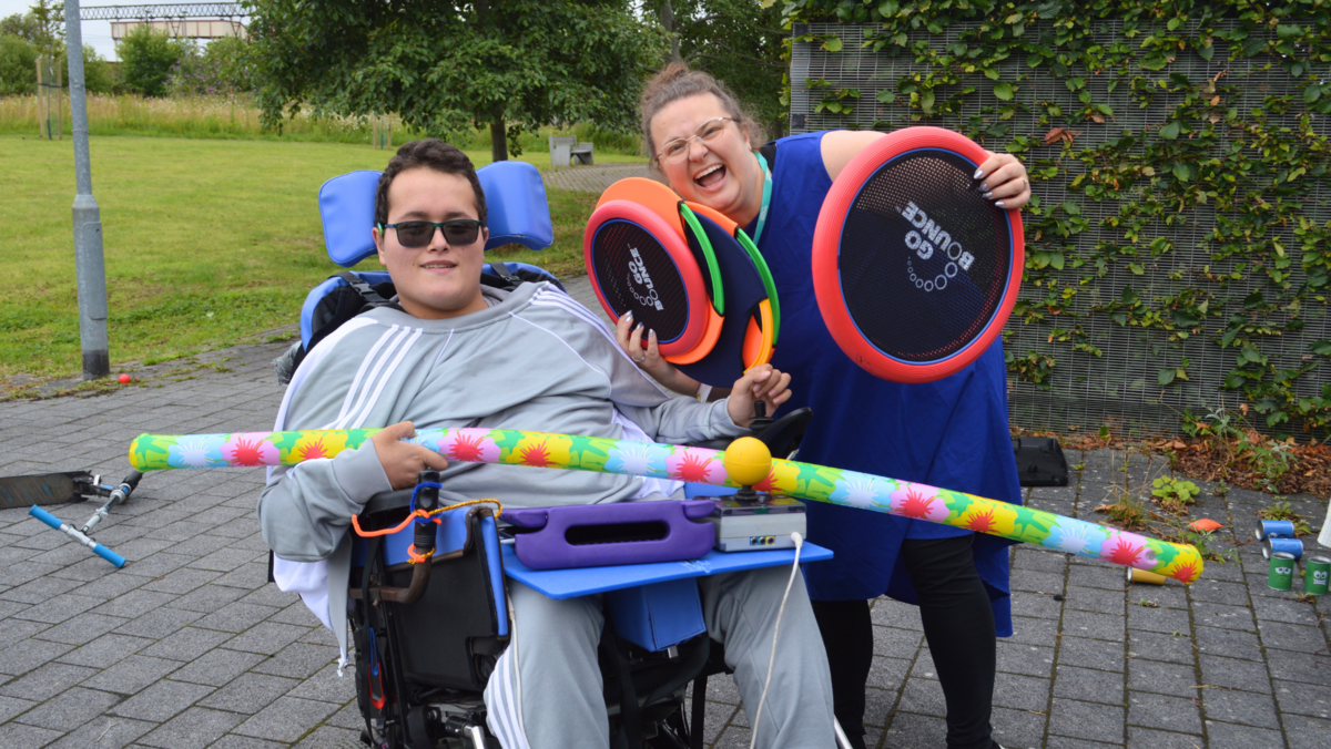 A Bridge student and member of staff getting ready to take part in some sport activities. Both smiling at the camera holding sports equipment 