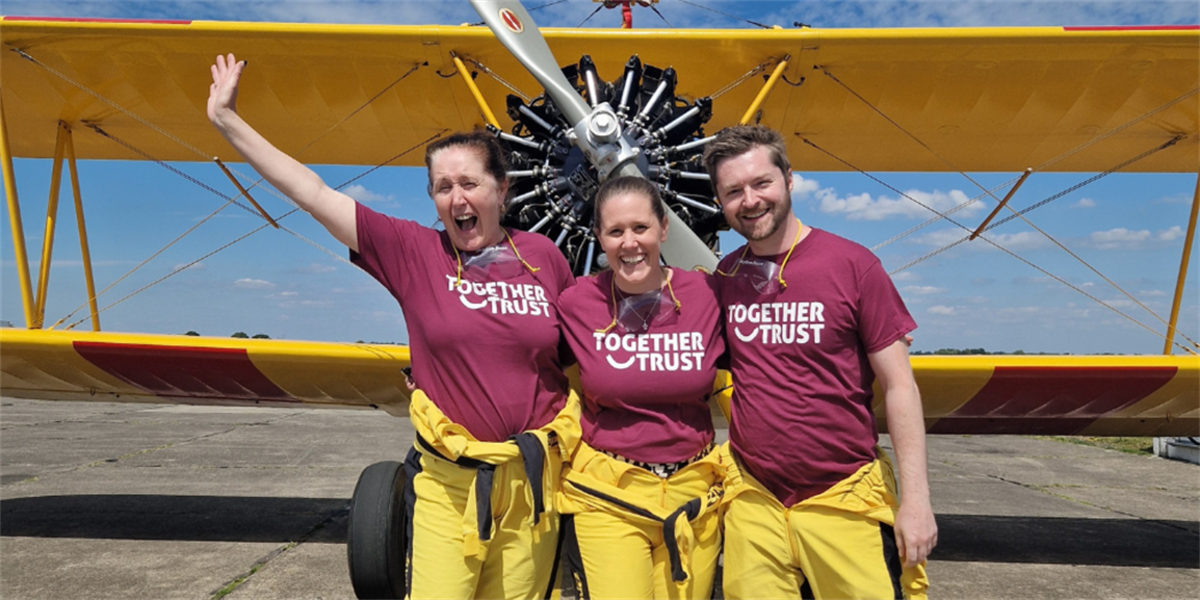 A snapshot of Lorraine, Shana, and Matt, donned in Together Trust's burgundy t-shirts. Their faces gleam with excitement, standing proudly before the plane.