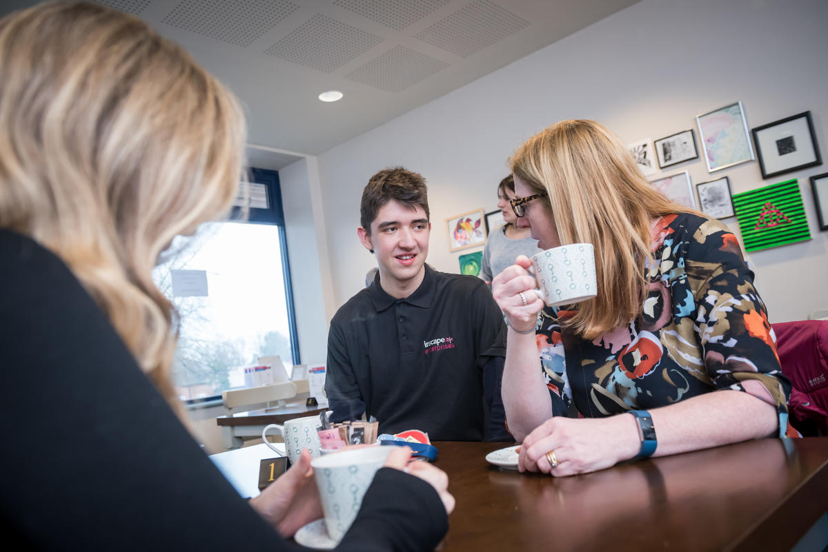 An Inscape student at inCafe, serving two women, enjoying their tea