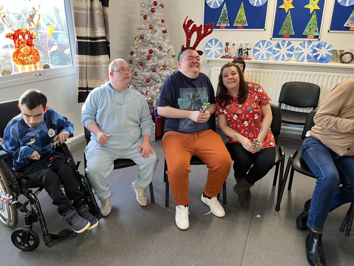 Group photo of staff member and 3 men smiling at the camera. There are christmas decorations in the background. 