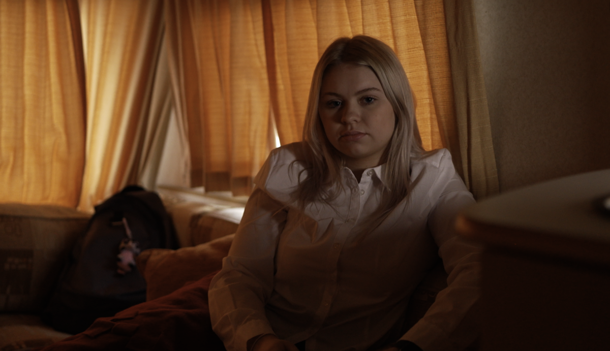 Teenager in school uniform sat in dimly lit caravan.