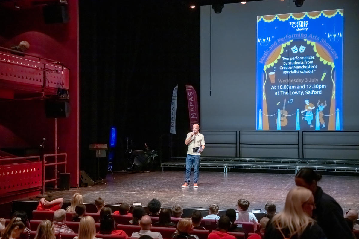 A theatre room full of people. A man is presenting on stage.