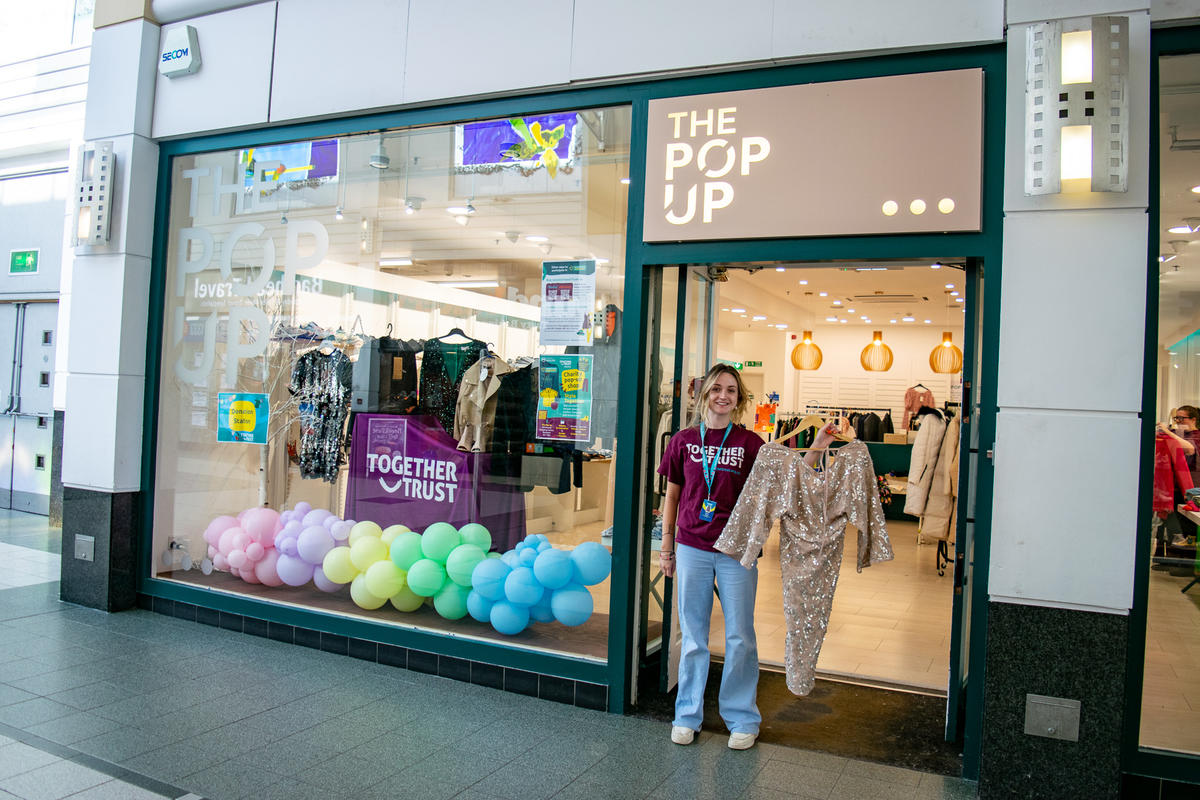 a woman in a together trust t shirt stood outside our pop up shop holding a dress on a hanger