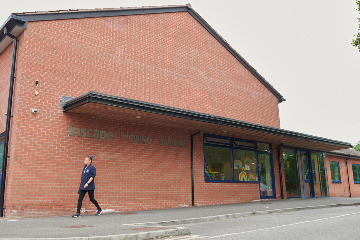 A staff member walks by a large brick building that says Inscape School across the side.