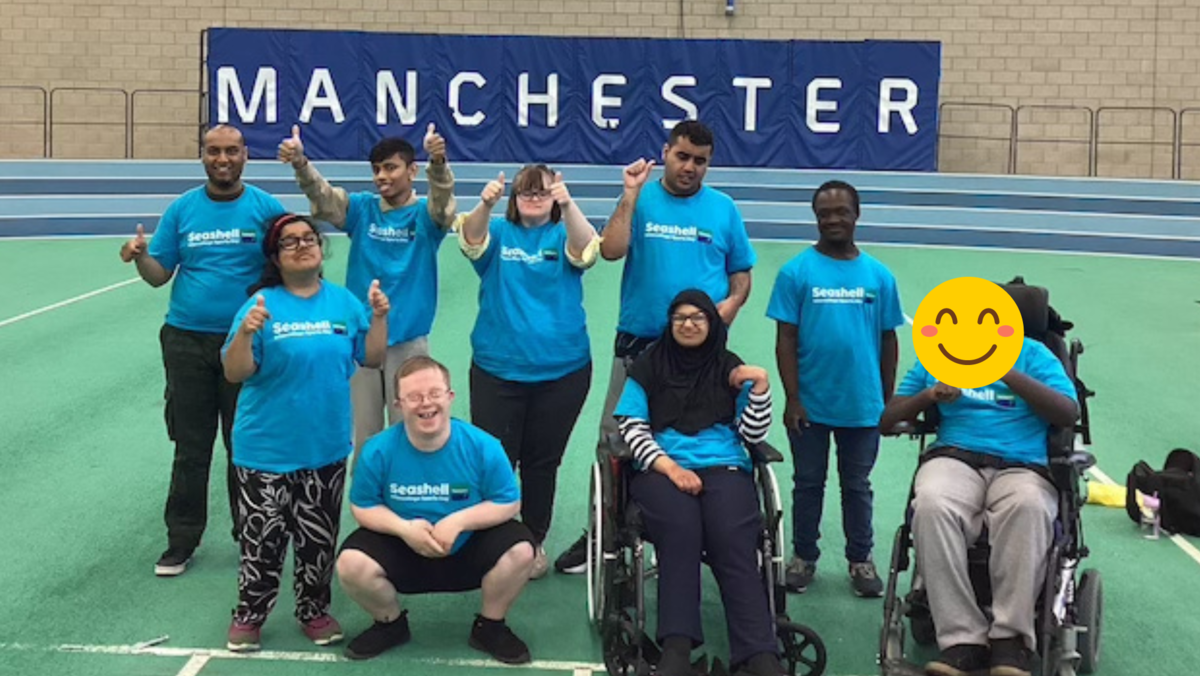 Students with thumbs up smiling at the camera underneath a 'Manchester' banner