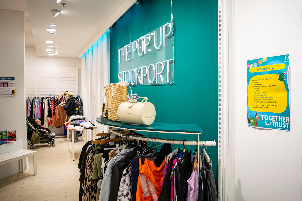 Rows of clothes and bags for sale under a neon 'pop up shop' sign.