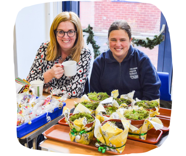 Two teachers smiling behind of a table of decorated plant pots. 