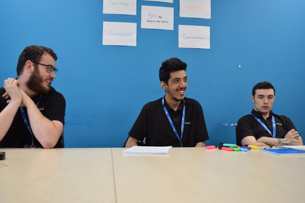 three students sitting at a table smiling at each other