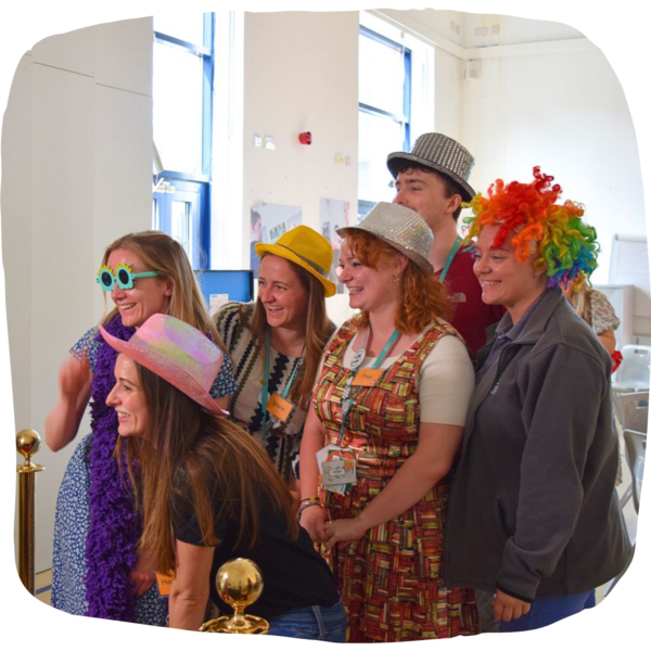 Students and staff posing in funky hats and wigs at the end of term celebrations.