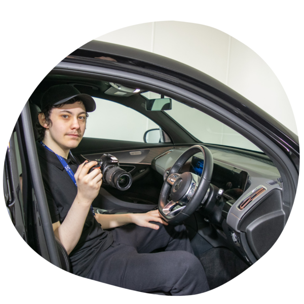 Student sat in a car with a camera during a tour of a local car dealer.