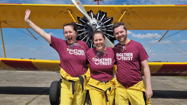 A snapshot of Lorraine, Shana, and Matt, donned in Together Trust's burgundy t-shirts. Their faces gleam with excitement, standing proudly before the plane.