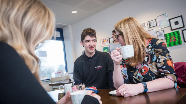 An Inscape student at inCafe, serving two ladies, enjoying their tea