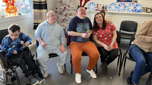 Group photo of staff member and 3 men smiling at the camera. There are christmas decorations in the background. 