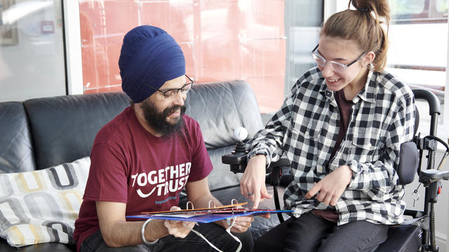 a staff member wearing a together trust t shirt showing a young woman in a wheelchair something on an iPad