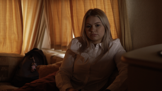 Teenager in school uniform sat in dimly lit caravan.