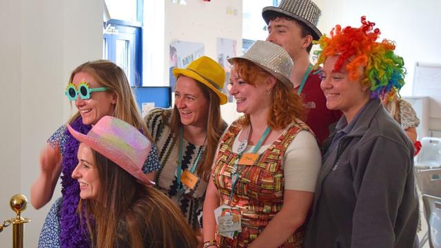 Students and staff posing in funky hats and wigs at the end of term celebrations.