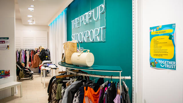 Rows of clothes and bags for sale under a neon 'pop up shop' sign.